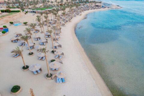 Flygbild över stranden på Blend Elphistone Resort, med palmer, halmparasoller och turkost hav