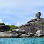 Det enorma balanserande granitblocket på ö 8 kröner en hög av släta grå klippor vid kanten av turkost vatten, under en disig blå himmel, med en rad bojar i förgrunden