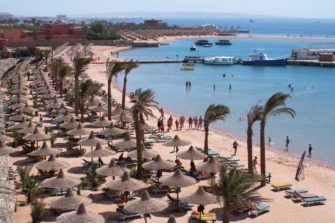 Stranden på Giftun Azur Resort, med halmparasoller och palmer, en brygga och båtar i bakgrunden