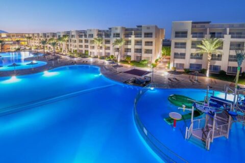 De upplysta poolerna på JAZ Soma Beach i skymningen, mellan byggnaderna och palmerna