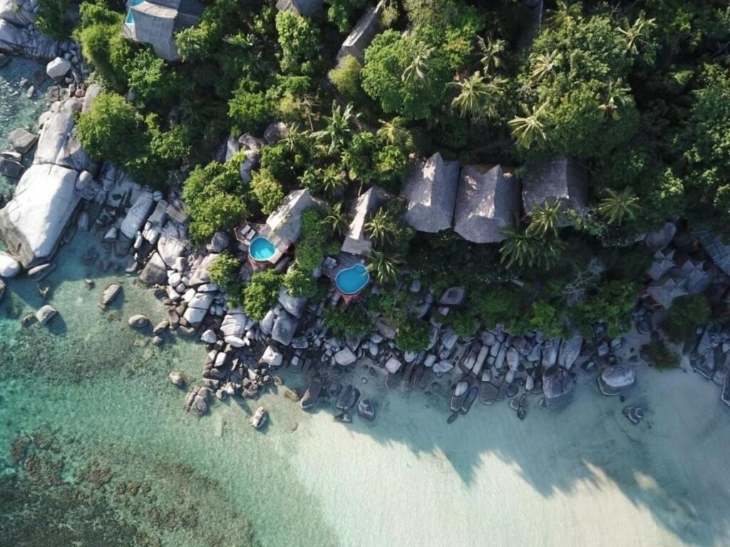 Flygbild över Koh Tao Cabana, med stugor bland träden, klippor och en vit sandstrand