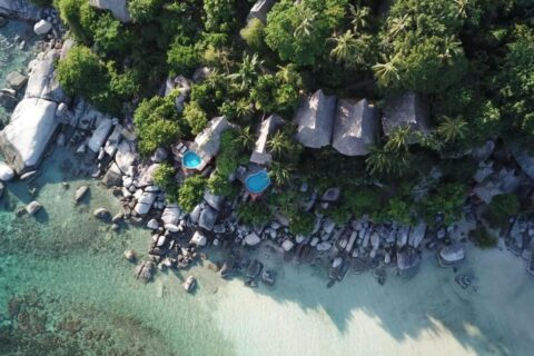 Flygbild över Koh Tao Cabana, med stugor bland träden, klippor och en vit sandstrand