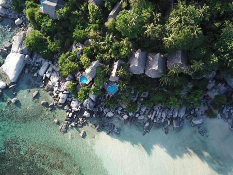 Flygbild över Koh Tao Cabana, med stugor bland träden, klippor och en vit sandstrand