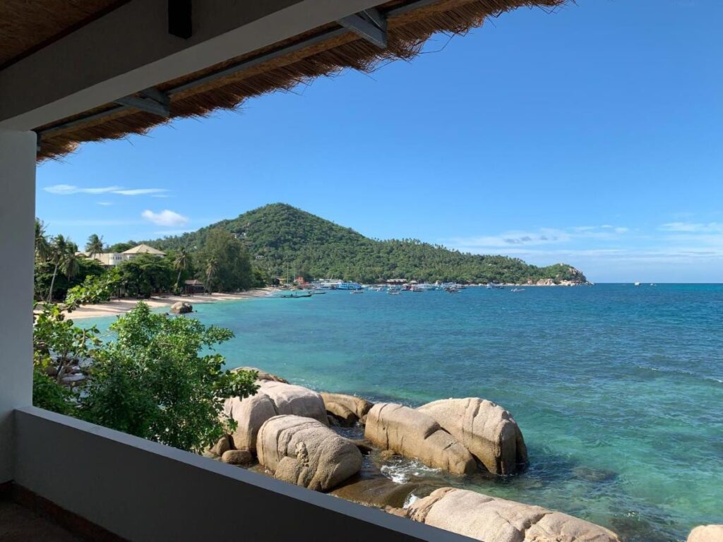 Bukten och klipporna sedda från en täckt terrass på Koh Tao Heritage, med båtar för ankar