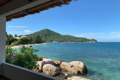 Bukten och klipporna sedda från en täckt terrass på Koh Tao Heritage, med båtar för ankar