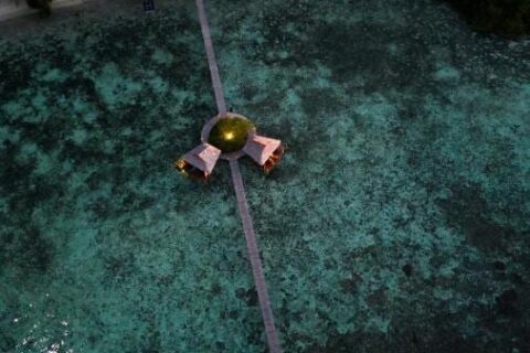 Flygbild nattetid av en lång träbrygga som går ut från stranden, med två hyddor på pålar halvvägs ut