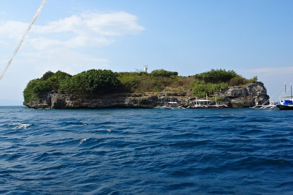 Pescador Island sedd från havet, täckt av gröna buskar, med den vita fyren på toppen och tre dykbåtar förtöjda vid foten av klippan