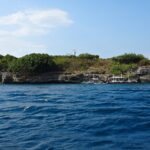 Pescador Island sedd från havet, täckt av gröna buskar, med den vita fyren på toppen och tre dykbåtar förtöjda vid foten av klippan