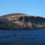 San Benedictos kust sedd från havet: vulkanen Bárcenas askkon, fårad av raviner, ovanför mörka klippor och ett mörkblått hav