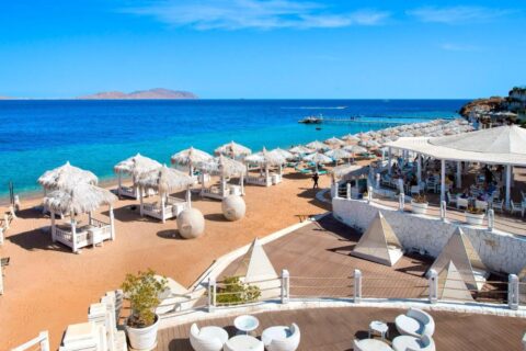 Stranden på Sunrise Arabian Beach Resort, med halmparasoller och brygga, mitt emot ön Tiran