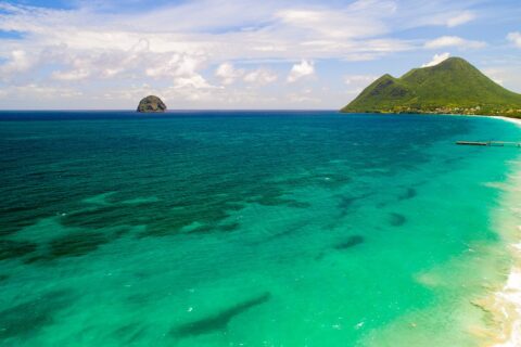 Flygbild av den långa stranden i Le Diamant kantad av turkost vatten, med Rocher du Diamant ute i havet och Morne Larcher, en grön kulle, till höger
