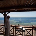 Från en träterrass ser en man i galabeya ut över bassängen i Blue Hole, kantad av ljust rev, där badare simmar
