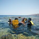 Simmare i gula västar, med mask och snorkel, i det klara vattnet i Blue Hole, med Sinais berg i bakgrunden